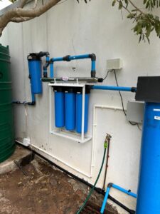Spritza borehole filtration system with blue cylindrical filter housings, black piping, and a white manifold, supporting water testing to meet SANS 241 requirements